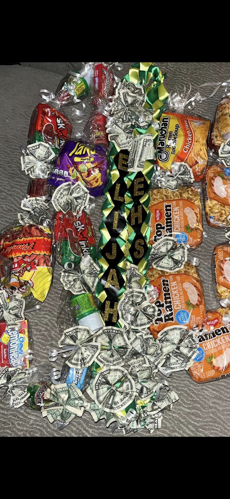 A cloth graduation lei with the grad's name, another lei made with candy and chips, and a third lei made with packages of instant ramen.